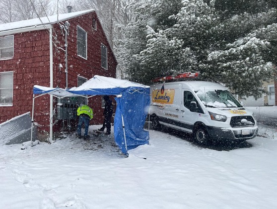 Landry Mechanical Van and installer installing heat pump on home while snowing outside