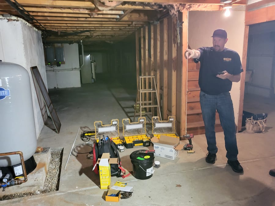 Landry technician in unfinished basement conducting plumbing construction.