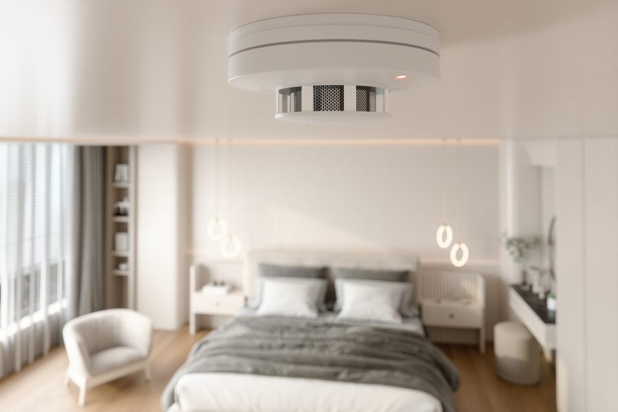 A smoke detector on the ceiling of a bedroom