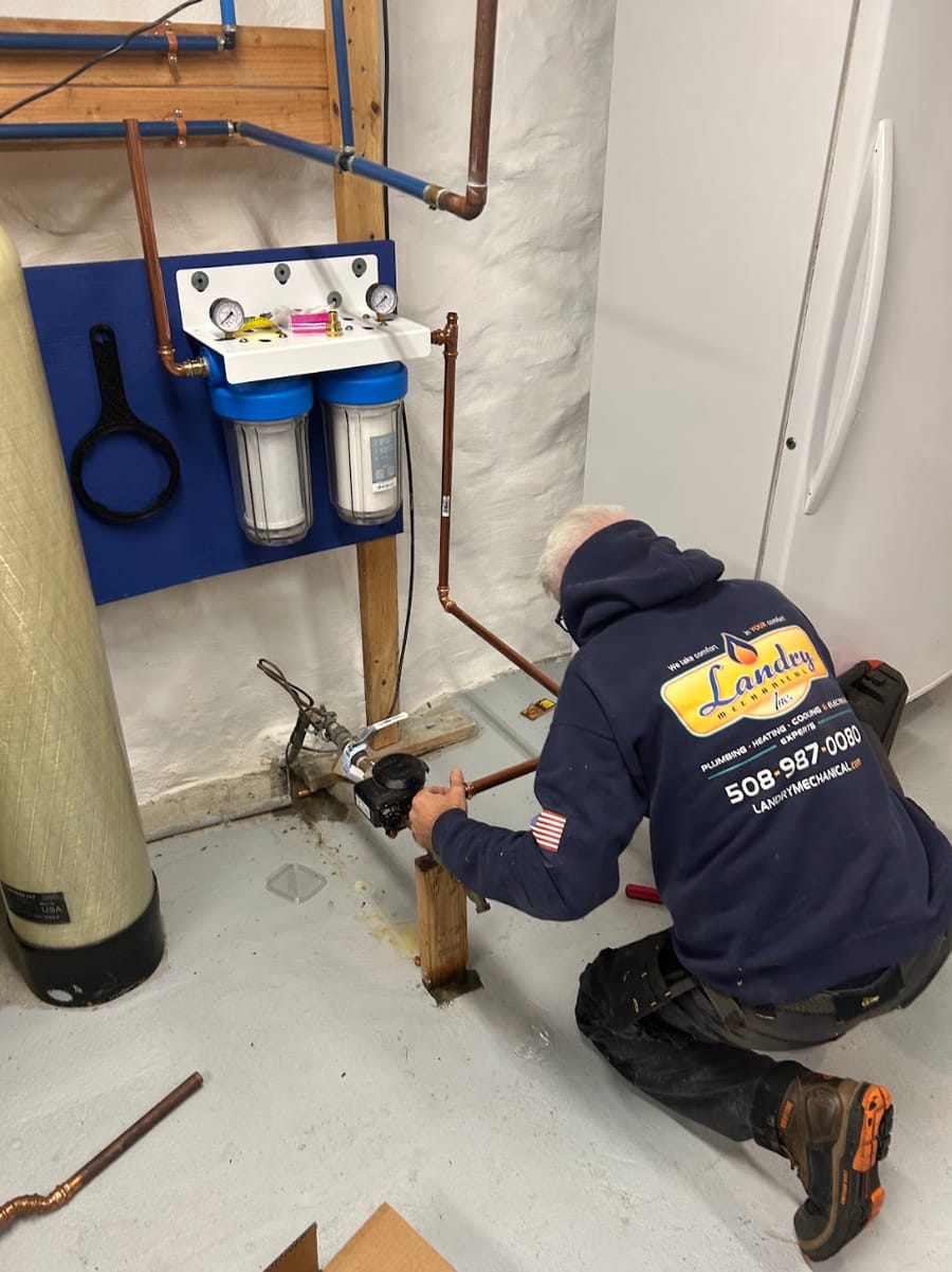 Plumber kneeling on ground installing water filtration system.
