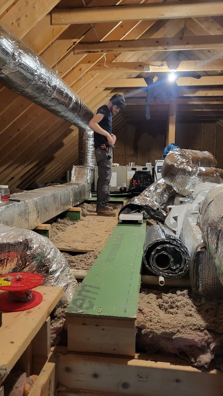 Landy technician standing in attic working on air ducts.