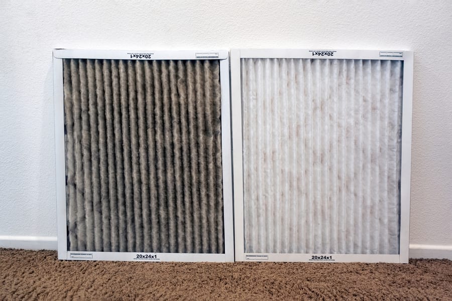 Two air filters resting against a wall, one dirty and one new.