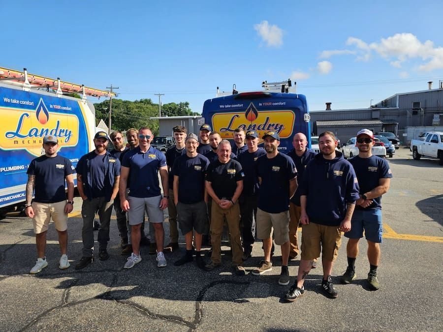 Group of Landry Mechanical technicians posing in front of blue company service trucks on a sunny day