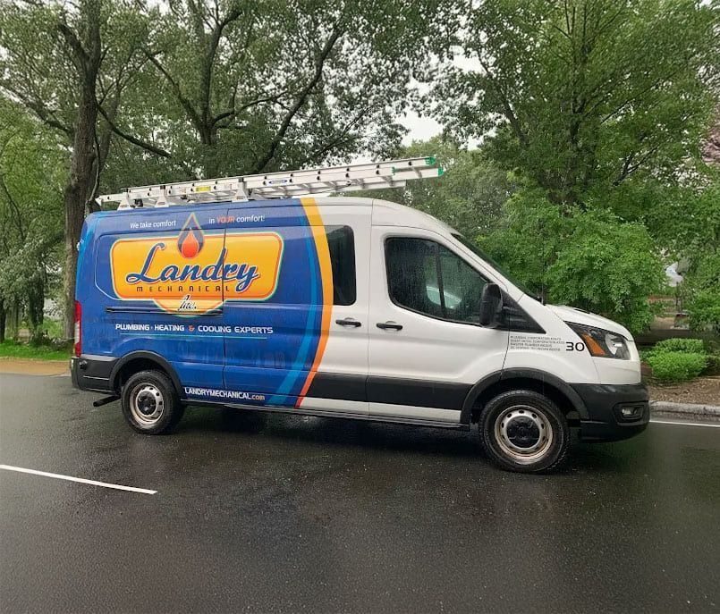 Landry Mechanical service van with blue and orange branding, ladder rack on top, parked on a wet street with green trees in the background.